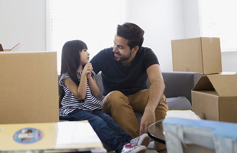 Father and daughter sitting in new living room with packed boxes